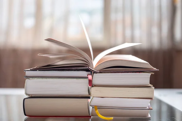 Nyitott könyv egy halom könyvet, egy asztal, egy világos szobában. Oktatás és olvasó könyv könyvek — Stock Fotó