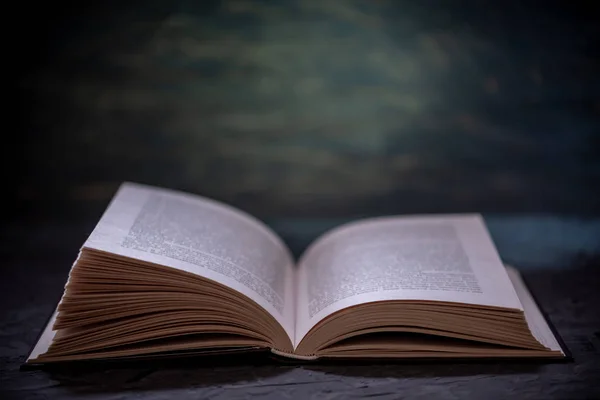 Nyitott könyv egy halom könyvet, egy asztal, egy sötét háttér. Oktatás és olvasó könyv könyvek — Stock Fotó
