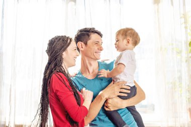 Mutlu anne baba ve anne pencere arka planda bebek oğlu ile oynarken. Neşeli ve modern genç aile