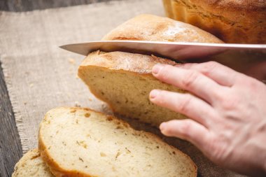 Eller ahşap arka plan üzerinde altın bir kabuk ile bir bıçak ev yapımı doğal taze ekmek ile kesilmiş. Fırın ürünleri