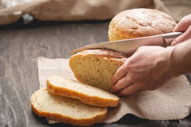 Eller ahşap arka plan üzerinde altın bir kabuk ile bir bıçak ev yapımı doğal taze ekmek ile kesilmiş. Fırın ürünleri