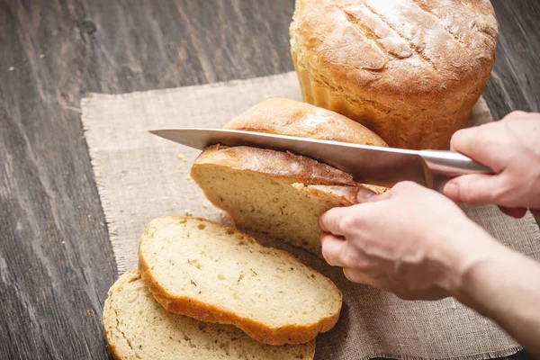Eller ahşap arka plan üzerinde altın bir kabuk ile bir bıçak ev yapımı doğal taze ekmek ile kesilmiş. Fırın ürünleri