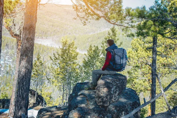 Muž s velkým batohu sedí na skalním útesu a dívá se na rozlehlé zelené údolí. Svoboda cestování — Stock fotografie