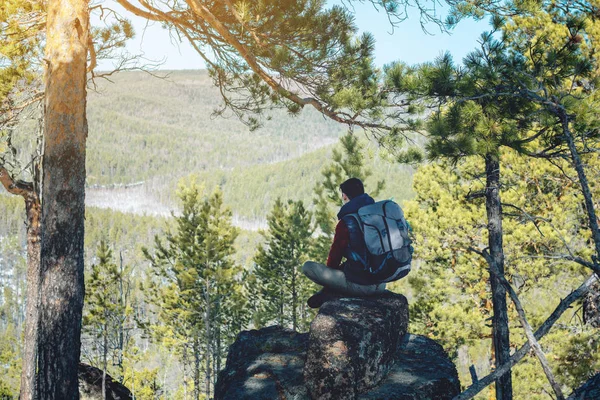 바위 절벽에 앉아 거대한 녹색 계곡을 바라보는 큰 배낭을 가진 남자 등산객. 여행의 자유 — 스톡 사진