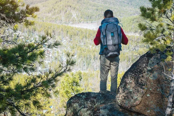 Turista uomo con un grande zaino si erge su una scogliera rocciosa e guardando la valle verde tentacolare. Libertà di viaggio — Foto Stock