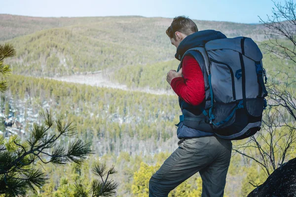 Ein Mann mit einem großen Rucksack steht auf einer Felswand und blickt auf das weitläufige grüne Tal. Reisefreiheit — Stockfoto
