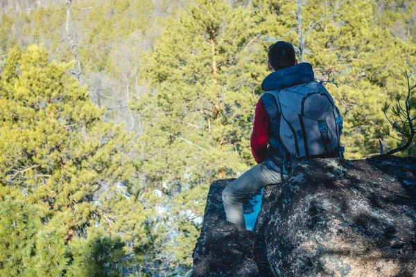 Muž s velkým batohu sedí na skalním útesu a dívá se na rozlehlé zelené údolí. Svoboda cestování — Stock fotografie