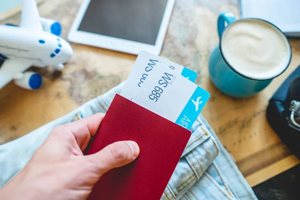 Mão segurando um passaporte e dois bilhetes no fundo da câmera, o mapa do mundo. Preparação para a viagem — Fotografia de Stock