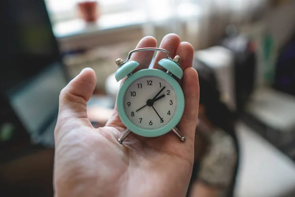 Reloj despertador analógico azul en mano sobre fondo de habitación. Concepto de tiempo y tarde para el trabajo — Foto de Stock