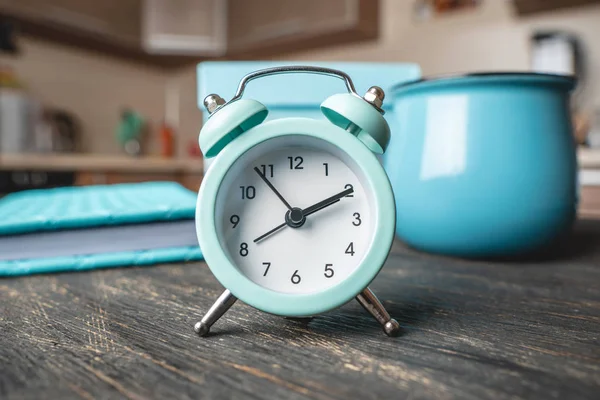 Reloj despertador de metal azul en la mesa con una taza y un diario en el fondo de la cocina. Tiempo y modo hogar — Foto de Stock