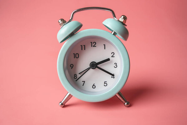 Синий аналоговый металлический будильник на стильном розовом фоне. Концепция времени в пастельных цветах
