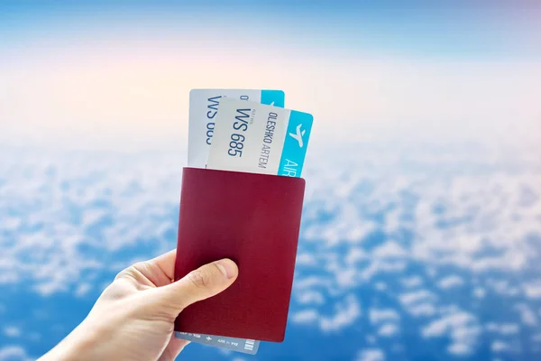 Mano con pasaporte y dos pasajes aéreos sobre un fondo azul de cielo nublado. Viajes y vacaciones en lugares hermosos — Foto de Stock