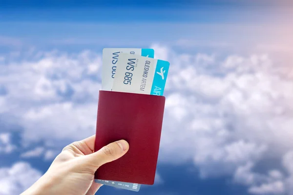 Χέρι κρατώντας ένα διαβατήριο και δύο αεροπορικά εισιτήρια σε ένα γαλάζιο φόντο συννεφιασμένο ουρανό. Ταξίδια και διακοπές σε όμορφα μέρη — Φωτογραφία Αρχείου