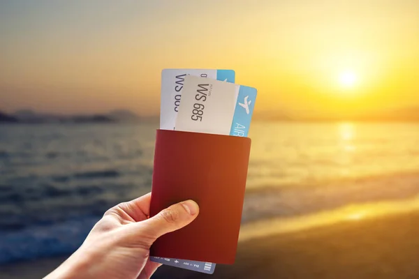 Ręka trzyma paszport i dwa bilety lotnicze na niebieskim tle morza. Podróże i urlop w egzotycznych miejscach — Zdjęcie stockowe
