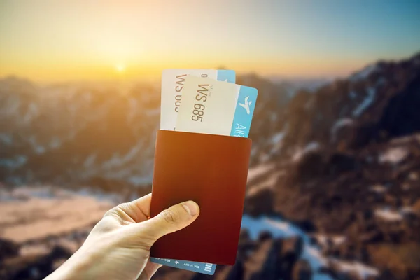 In der Hand einen Pass und zwei Flugtickets vor blauem Hintergrund der Berge. Reisen und Urlaub an schönen Orten — Stockfoto