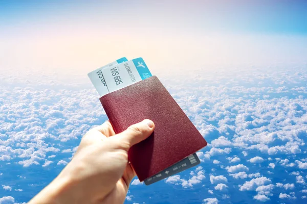 Рука с паспортом и двумя билетами на голубом фоне облачного неба. Путешествия и отдых в красивых местах — стоковое фото