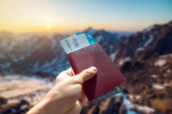 Mano con pasaporte y dos pasajes aéreos sobre un fondo azul de montañas. Viajes y vacaciones en lugares hermosos — Foto de Stock
