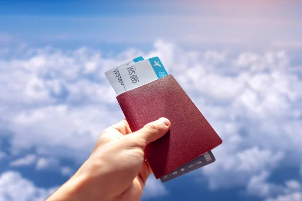 Mano con pasaporte y dos pasajes aéreos sobre un fondo azul de cielo nublado. Viajes y vacaciones en lugares hermosos — Foto de Stock