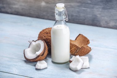 Mavi ahşap arka plan üzerinde beyaz et ile bir şişe hindistan cevizi sütü. Kozmetolojide kullanılan organik ürün