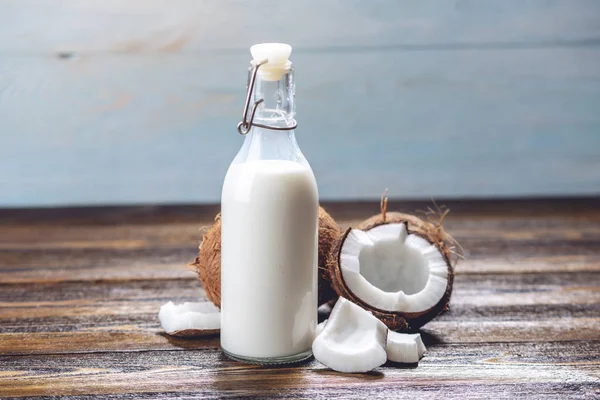 Leche de coco en una botella con carne blanca sobre un fondo de madera. Producto orgánico saludable utilizado en cosmetología — Foto de Stock