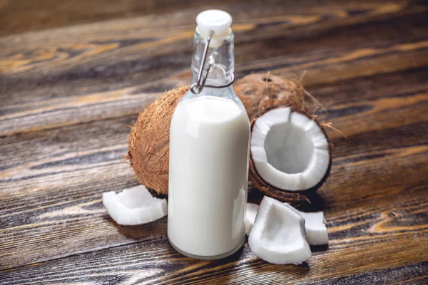 Ahşap bir arka plan üzerinde beyaz et ile bir şişe hindistan cevizi sütü. Kozmetolojide kullanılan organik sağlıklı ürün