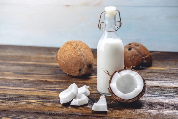 Ahşap bir arka plan üzerinde beyaz et ile bir şişe hindistan cevizi sütü. Kozmetolojide kullanılan organik sağlıklı ürün