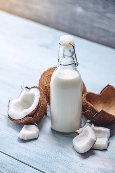 Leche de coco en una botella con carne blanca sobre un fondo de madera azul. Producto orgánico saludable utilizado en cosmetología — Foto de Stock