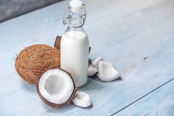 Mavi ahşap arka plan üzerinde beyaz et ile bir şişe hindistan cevizi sütü. Kozmetolojide kullanılan organik sağlıklı ürün