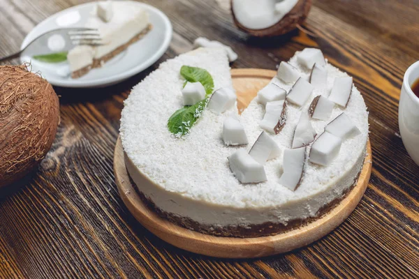 Raw coconut cake decorated with white coconut pulp and mint on a wooden background. Healthy vegan dessert.