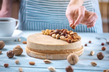 Ahşap bir arka plan üzerinde ceviz, badem, fındık ve macadamia tepesi ile Nutty karamel cheesecake.