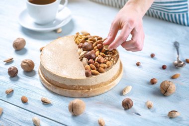 Ahşap bir arka plan üzerinde ceviz, badem, fındık ve macadamia tepesi ile Nutty karamel cheesecake.