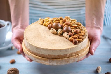 Ahşap bir arka plan üzerinde ceviz, badem, fındık ve macadamia tepesi ile Nutty karamel cheesecake.