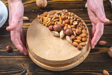 Koyu ahşap arka plan üzerinde ceviz, badem, fındık ve macadamia tepesi ile Nutty karamel cheesecake kek.