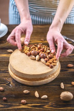 Koyu ahşap arka plan üzerinde ceviz, badem, fındık ve macadamia tepesi ile Nutty karamel cheesecake kek.