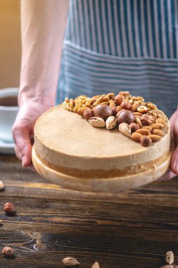 Koyu ahşap arka plan üzerinde ceviz, badem, fındık ve macadamia tepesi ile Nutty karamel cheesecake kek.