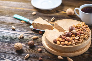 Koyu ahşap arka plan üzerinde ceviz, badem, fındık ve macadamia tepesi ile Nutty karamel cheesecake kek.