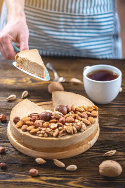 Koyu ahşap arka plan üzerinde nutty cheesecake. Mavi önlüklü şekerlemeci bir parça fındıklı kek tutarken