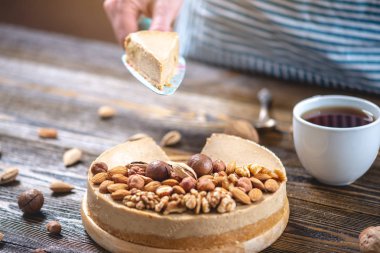 Koyu ahşap arka plan üzerinde nutty cheesecake. Mavi önlüklü şekerlemeci bir parça fındıklı kek tutarken