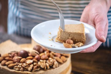 Koyu ahşap arka plan üzerinde nutty cheesecake. Mavi önlüklü şekerlemeci bir parça fındıklı kek tutarken