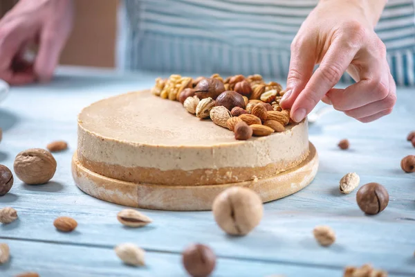 Ahşap bir arka plan üzerinde ceviz, badem, fındık ve macadamia tepesi ile Nutty karamel cheesecake.