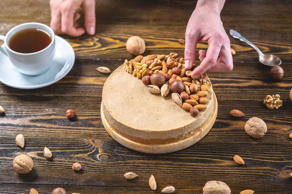 Koyu ahşap arka plan üzerinde ceviz, badem, fındık ve macadamia tepesi ile Nutty karamel cheesecake kek.