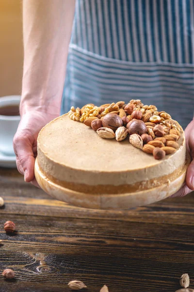 Koyu ahşap arka plan üzerinde ceviz, badem, fındık ve macadamia tepesi ile Nutty karamel cheesecake kek.