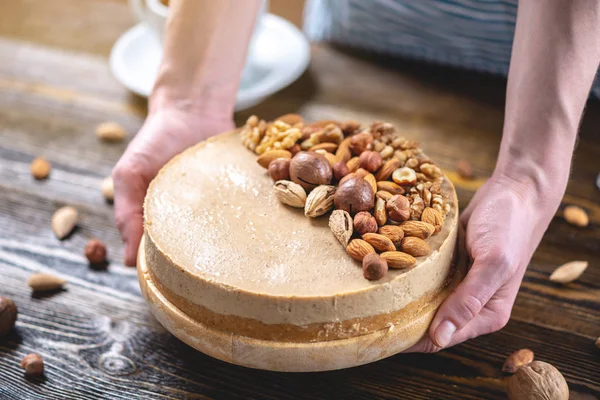 Koyu ahşap arka plan üzerinde ceviz, badem, fındık ve macadamia tepesi ile Nutty karamel cheesecake kek.