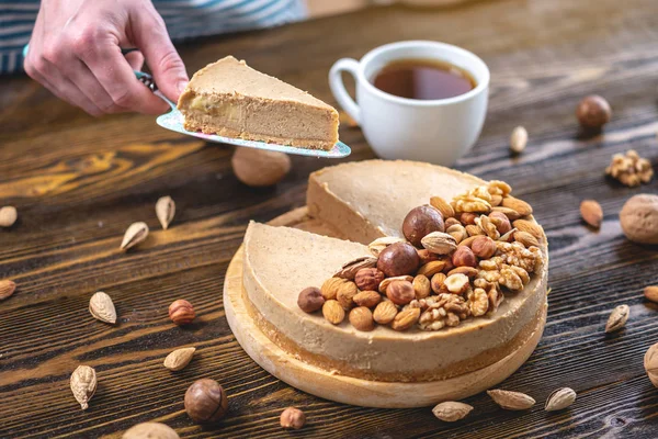Koyu ahşap arka plan üzerinde nutty cheesecake. Mavi önlüklü şekerlemeci bir parça fındıklı kek tutarken