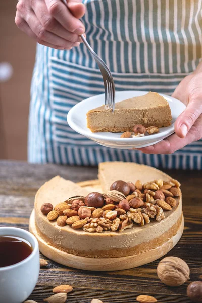 Koyu ahşap arka plan üzerinde nutty cheesecake. Mavi önlüklü şekerlemeci bir parça fındıklı kek tutarken
