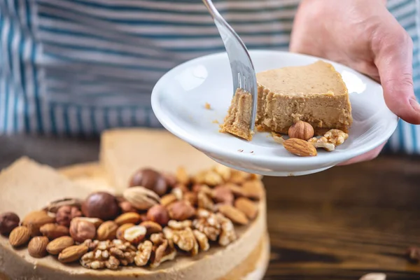Koyu ahşap arka plan üzerinde nutty cheesecake. Mavi önlüklü şekerlemeci bir parça fındıklı kek tutarken