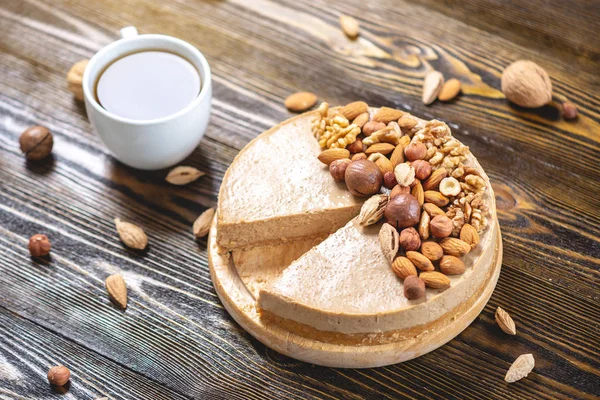 Koyu ahşap arka plan üzerinde ceviz, badem, fındık ve macadamia tepesi ile Nutty karamel cheesecake kek.