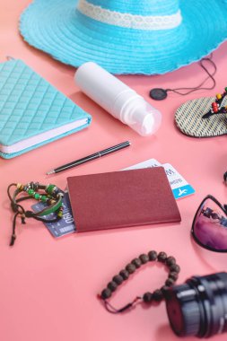 Seyahat tatil malzemeleri: şapka, güneş gözlüğü, kamera, pasaport ve pembe arka plan üzerinde uçak biletleri. Üst te. Düz yatıyordu