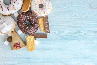 Mavi ahşap arka plan üzerinde Zararlı tatlı gıdalar. Masanın üstünde çörekler ve kekler var. Sağlıksız diyet ve kilolu