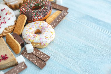 Mavi ahşap arka plan üzerinde Zararlı tatlı gıdalar. Masanın üstünde çörekler ve kekler var. Sağlıksız diyet ve kilolu